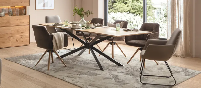 Elegantes Esszimmer mit großem Massivholztisch in Naturoptik, modernen Polsterstühlen in Braun und Beige und stilvoll gedecktem Tisch, mit Blick in den Garten durch große Fensterfront.